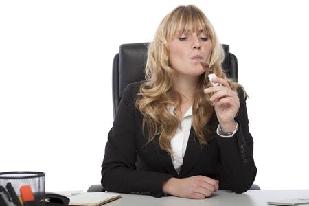 Attractive young businesswoman with long blond hair sitting at her desk enjoying a chocolate bar at work with a look of pleased anticipationの写真素材