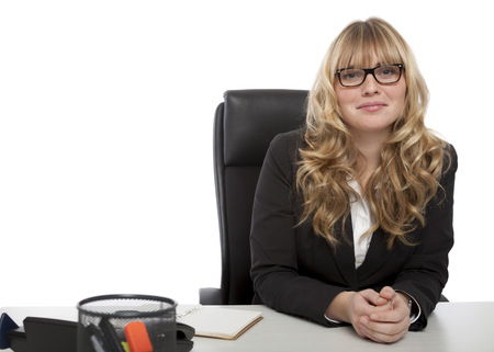 Smiling confident attractive young businesswoman in glasses sitting relaxing at her desk looking at the camera with a friendly smileの写真素材