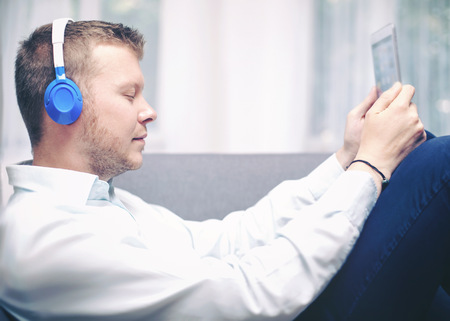 young stylish bearded man listening to music, while relaxing on couch with tablet pc, with special colour filter styleの写真素材