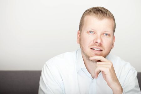 Pensive attractive young man sitting with his hand to his chin gazing thoughtfully at the camera, with copyspaceの写真素材