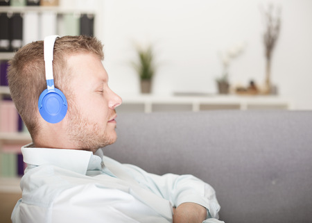 Young man enjoying his music sitting with folded arms and closed eyes listening to the tunes on his headphones, profile view indoorsの写真素材