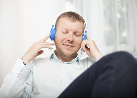 Man closing his eyes in bliss with an expression of enjoyment as he listens to music on a set of headphone while relaxing on a sofaの写真素材