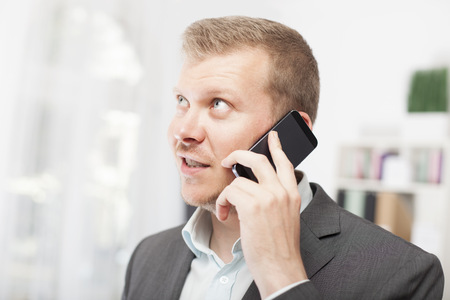 Businessman listening with anticipation to a call on his mobile phone standing looking up into the air with parted lipsの写真素材