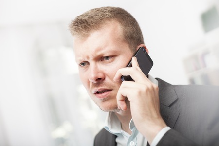 Anxious businessman taking a mobile phone call frowning with a worried expression as he listens to the conversationの写真素材