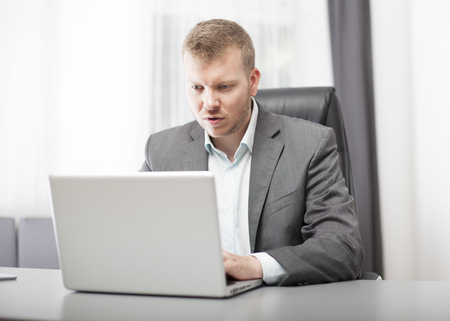 Businessman looking at his laptop in disbelief with a puzzled shocked expression as he digests the information on the screenの写真素材