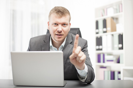 Businessman delivering a lecture to a client or colleague leaning forwards over his desk with an earnest expression shaking his fingerの写真素材