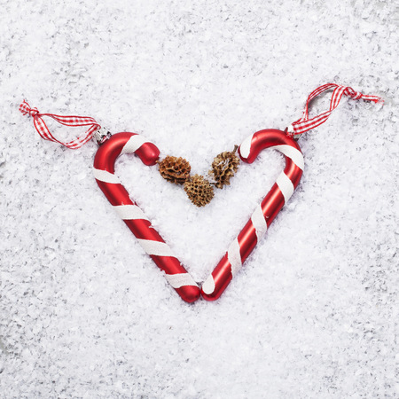 Two Candy Canes in Heart with Red ribbon on White snow Background.の写真素材