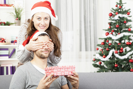 young girl is giving her boyfriend a christmas gift in front of christmas treeの写真素材