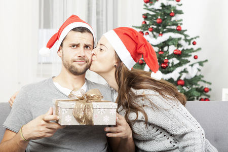 man is sceptical about christmas gift  while his girlfriend give him a kissの写真素材