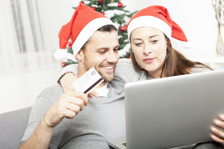 happy couple find perfect present gifts online on sofa indoors using credit card and laptopの写真素材