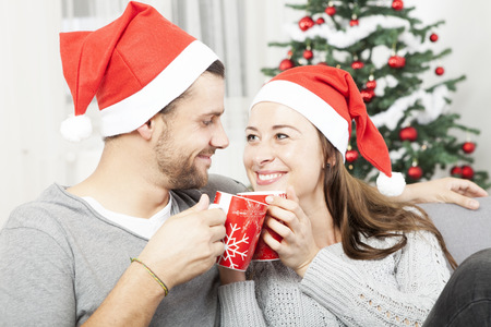 young christmas couple relaxing and enjoying hot tee or coffee on sofa and smileの写真素材