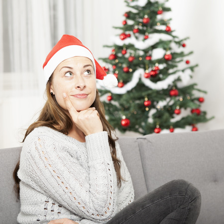 young pensive girl think about christmas on sofa in front of christmas treeの写真素材