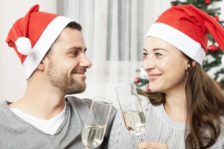 young christmas couple with champagne smiling in front od christmas tree, with red santa hatsの写真素材