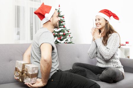 young man surprise girlfriend with gift for christmas with present box behind his backの写真素材