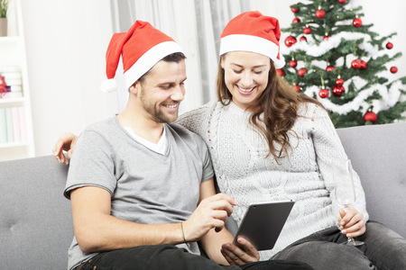 happy young couple use or watch something on tablet pc for christmas on sofaの写真素材