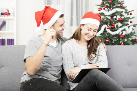 happy young couple makes a wish list for christmas an sofaの写真素材