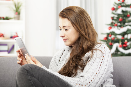 young girl sitting on sofa and surfing with tablet pc at christmasの写真素材