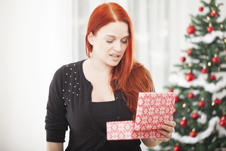 young red haired girl is really unhappy with gift box for christmasの写真素材