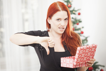 young red haired girl is really unhappy with gift box for christmas and thumbs downの写真素材