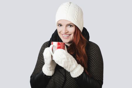 young wonderful girl with scarf and gloves and hot mug of tea, isolated on grey backgroundの写真素材