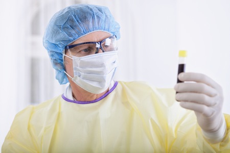 portrait of scientist or doctor in protective gear holding blood sampleの写真素材