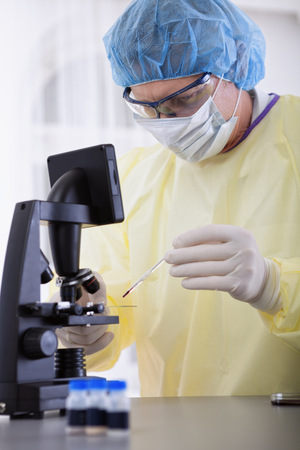 portrait of scientist or doctor in protective gear working with microscope and blood, in lab or hospitalの写真素材