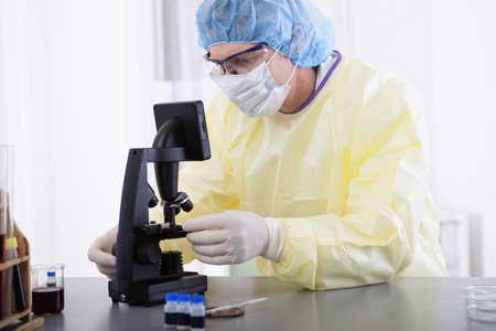 portrait of scientist or doctor in protective gear working with microscope and blood, in lab or hospitalの写真素材