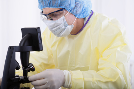 portrait of scientist or doctor in protective gear working with microscope and blood, in lab or hospitalの写真素材