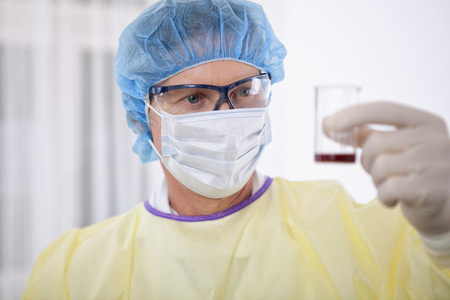 portrait of scientist or doctor in protective gear working with microscope and blood, in lab or hospitalの写真素材