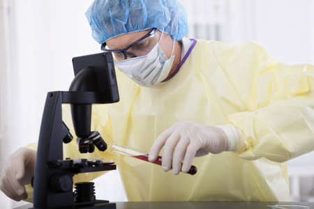 portrait of scientist or doctor in protective gear working with microscope and blood, in lab or hospitalの写真素材