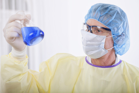 scientist working in the lab, in protective mask and cap, examines a test tube with liquidの写真素材
