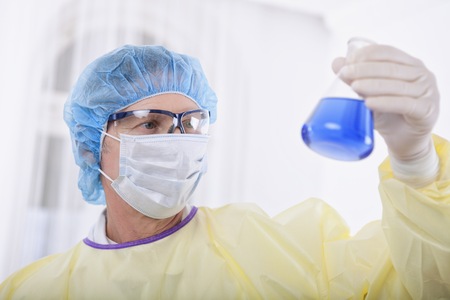 scientist working in the lab, in protective mask and cap, examines a test tube with liquidの写真素材