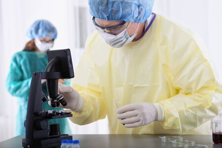 two scientist or doctors in protective gear working with microscope and blood, in lab or hospitalの写真素材
