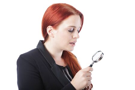 Attractive redhead woman holding a magnifying glass, profile view isolated on white in a conceptual imageの写真素材