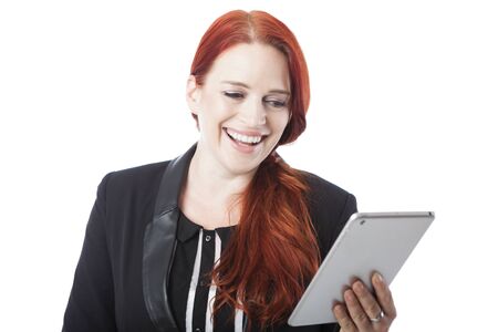 Stylish attractive redhead woman laughing with amusement as she reads her handheld tablet computer , upper body on whiteの写真素材