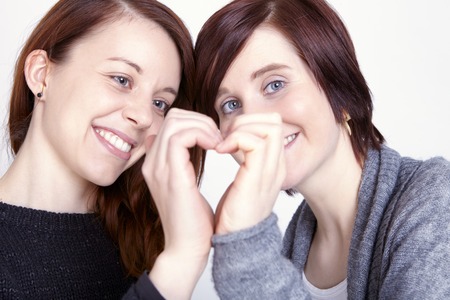 two girls friends make a heart with her hands on grey backgroundの写真素材