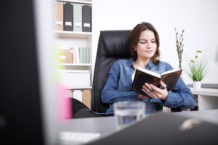 Young Office Woman in Denim Fashion Reading a Book Seriously While Sitting on her Chair at her Office.の写真素材