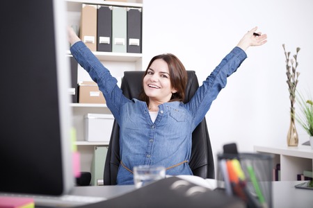 Happy Female Executive Sitting on her Chair at the Office While Stretching her Arms and Looking at the Camera.の写真素材