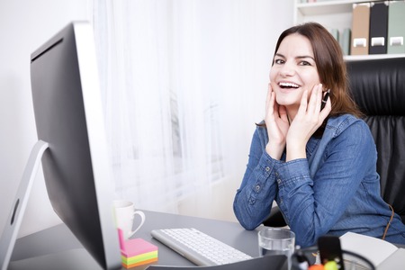 Happy Office Woman Leaning on the Table at her Office with Hands on her Face and Looking at the Camera.の写真素材