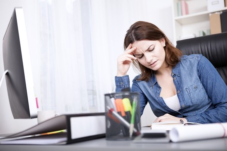 Close up Worried Young Businesswoman in Denim Blouse Sitting at her Office Table in the Office with Hand on her Forehead and Closed Eyes.の写真素材