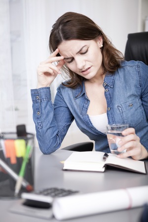 Close up Young Adult Office Woman Reading a Book Seriously While Holding a Glass of Water at her Deskの写真素材