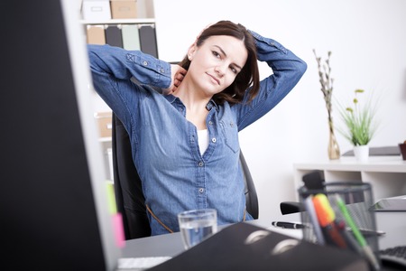Exhausted Young Office Woman Sitting at her Office, Holding her Head and Neck While Looking at Computer Screen.の写真素材