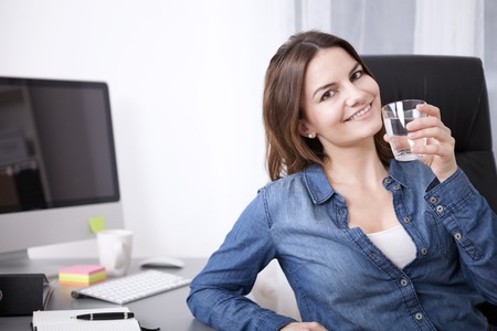 Close up Young Adult Office Woman Relaxing on her Chair While Holding a Glass of Water and Looking at the Camera.の写真素材