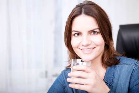Close up Portrait of a Happy Young Woman in Denim Outfit Holding a Glass of Water While Looking at the Camera.の写真素材