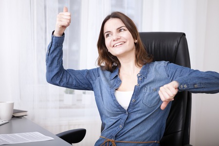 Undecided businesswoman laughing playfully and giving a thumbs up and down gesture simultaneouslyの写真素材