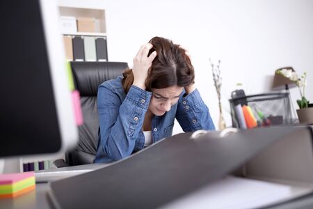 Hardworking dedicated businesswoman sitting at her desk in the office with her head in her hands concentrating on a paper document on the desk in front of herの写真素材