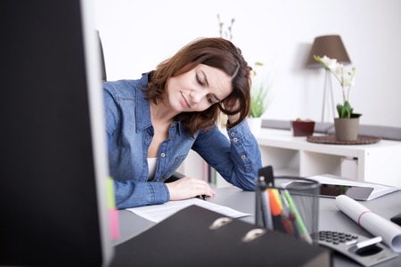 Attractive businesswoman working hard at the office sitting at her desk studying a paper document with a serious expression and her head resting on her handの写真素材