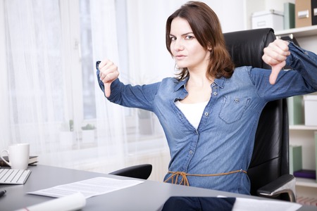 Businesswoman giving an emphatic thumbs down gesture with both hands and frowning at the camera depicting disapproval, a failure, voting something down or disagreementの写真素材