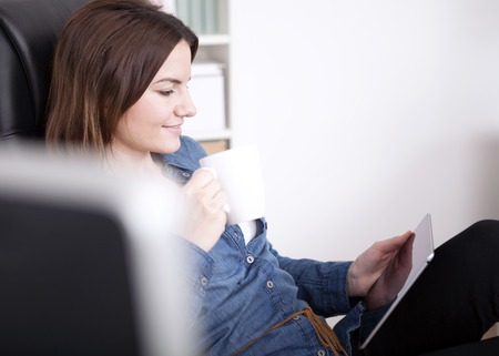Close up Pretty Young Office Woman Relaxing on her Office Chair with a Cup of Coffee and a Tablet Computerの写真素材