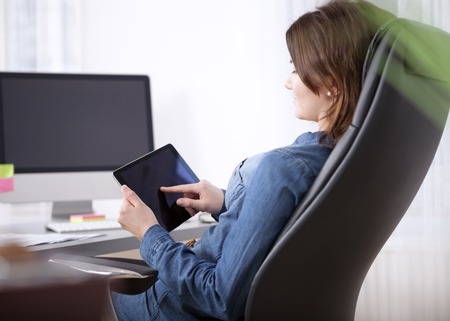 Close up Side View of an Office Woman Sitting at her Worktable Busy Browsing at her Tablet Computerの写真素材